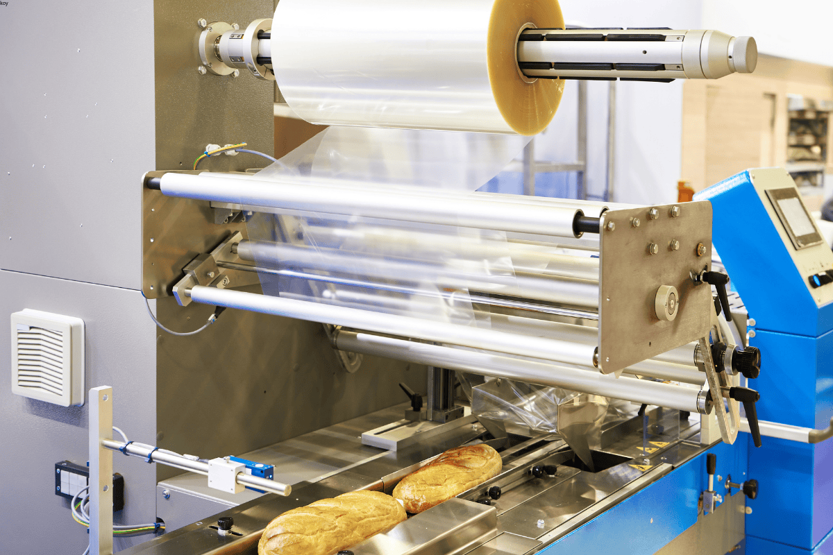 Automated flow wrapping machine using roll stock film to pack bakery products like bread