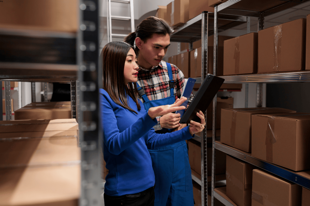 Two warehouse staff managing inventory with a tablet in a packaging facility
