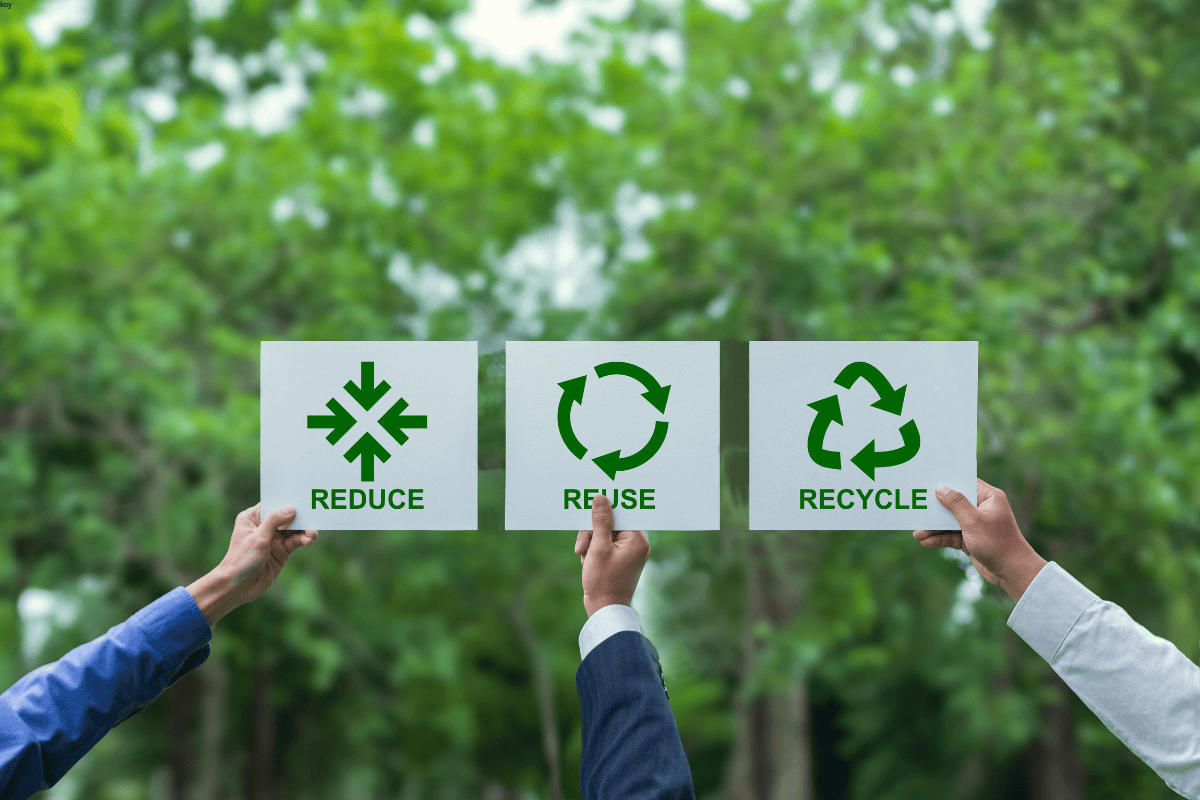 Hands holding signs with reduce, reuse, recycle symbols in nature