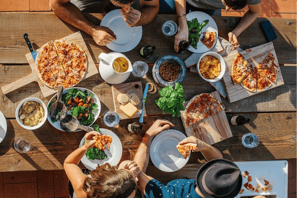 Group of people enjoying pizza, salad, and snacks together outdoors, representing food sharing and packaging use in real-life dining scenarios.