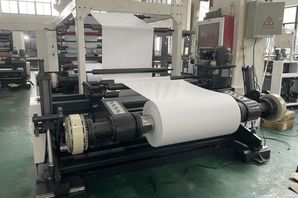 Roll stock slitting machine cutting large laminated paper rolls according to customer specifications in a Chinese packaging factory.